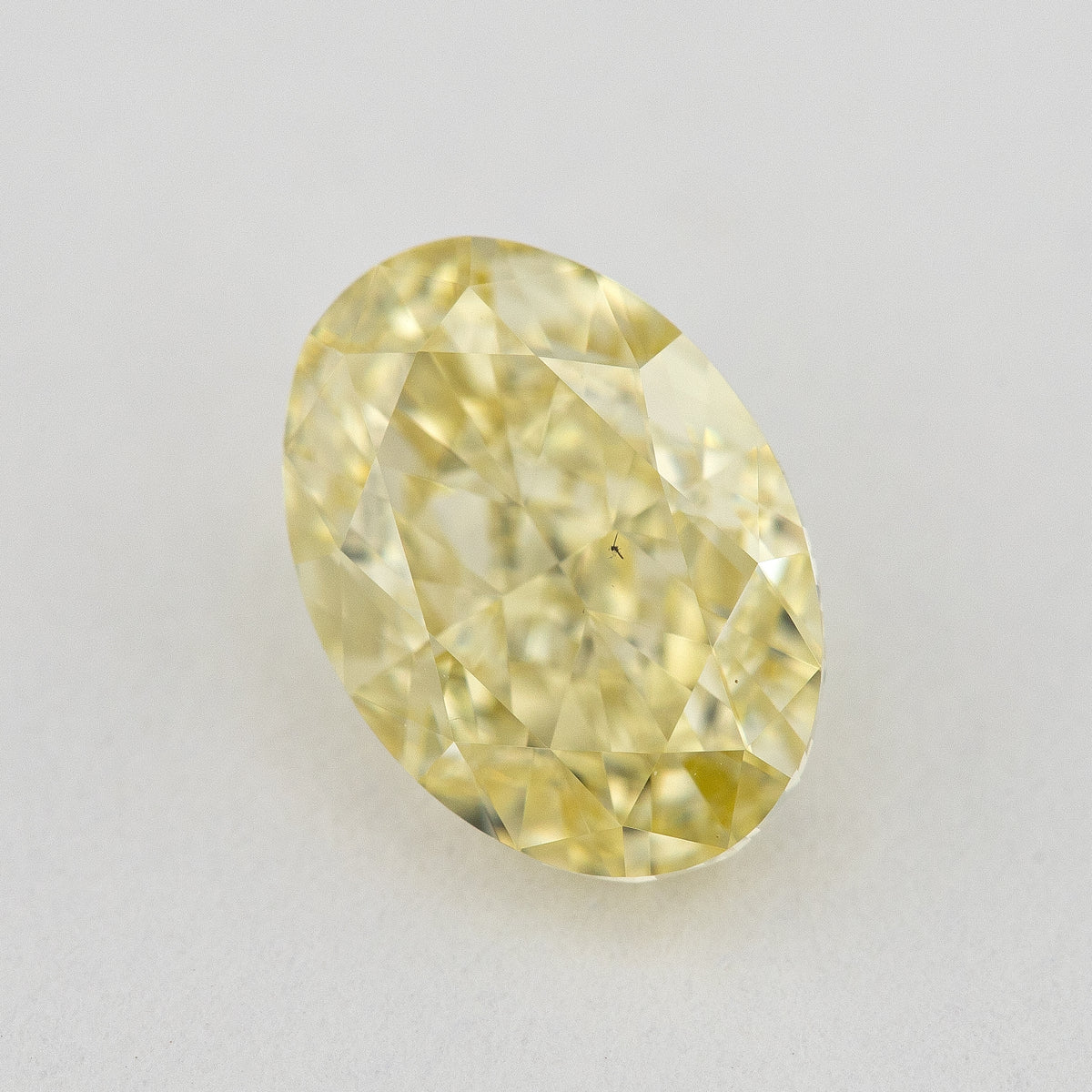 Alternate angled face-up view of the yellow oval diamond on a pale background, with a different pattern of light and dark facet reflections.