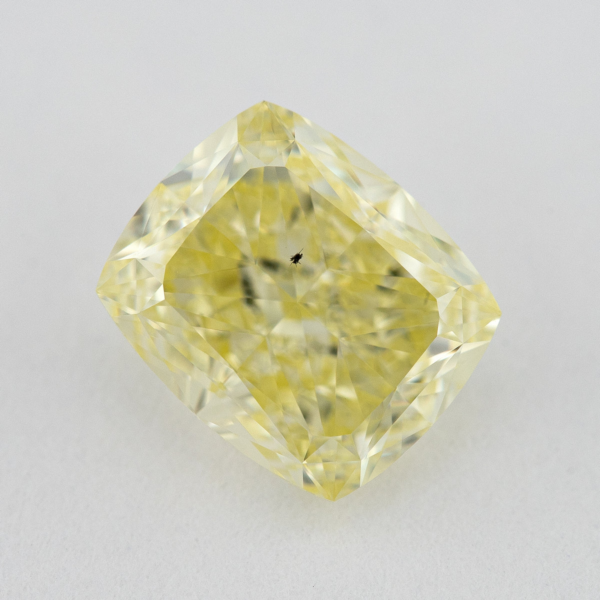 Face-up close-up of the yellow cushion diamond on a pale background, showing its complete outline and crown facet reflections.