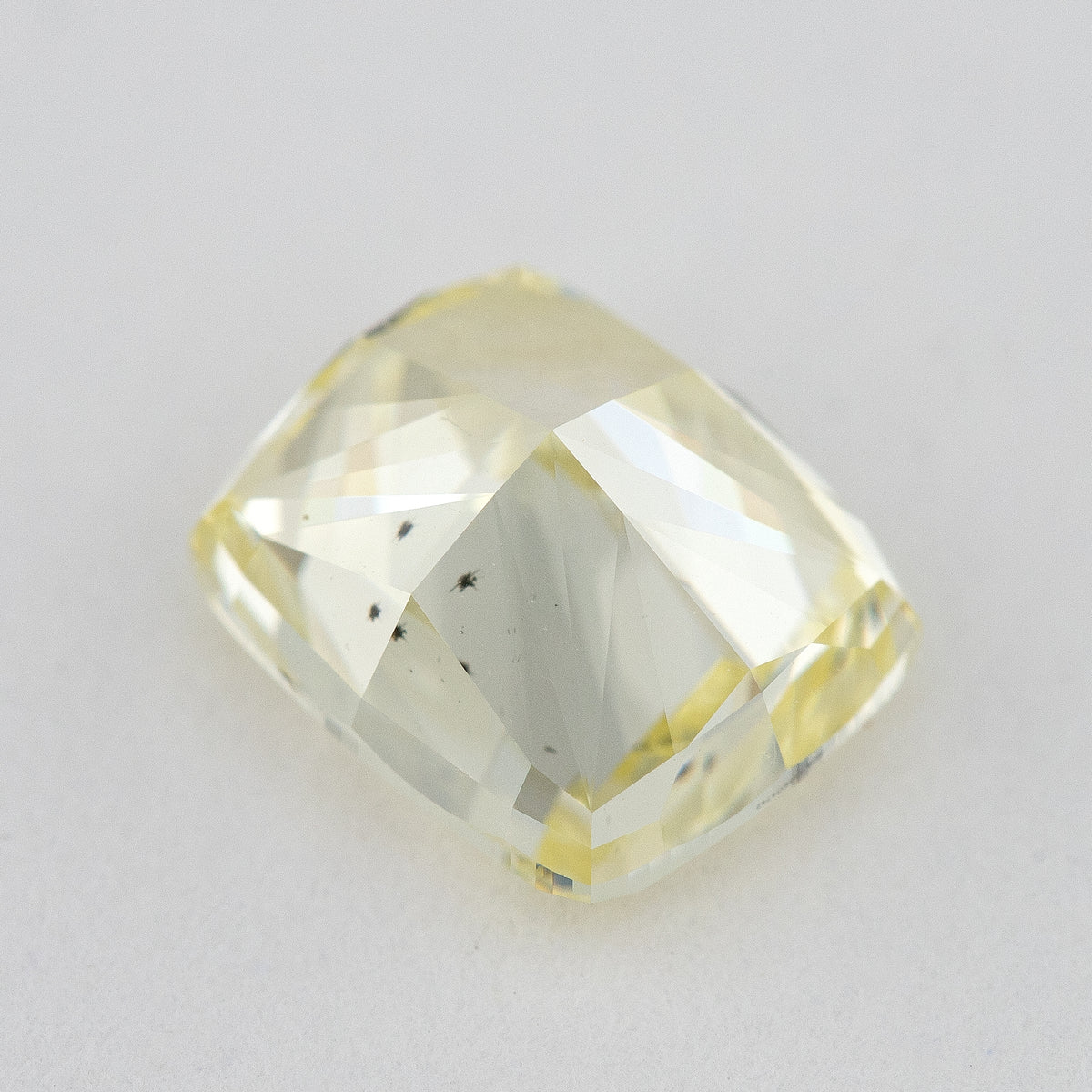 Low tilted view of the yellow cushion diamond, showing broad pavilion facets and the depth below its crown.