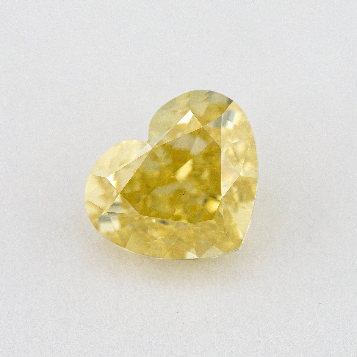 Heart-shaped yellow natural diamond face-up on a pale surface, with its lobes, point and broad crown facets visible.