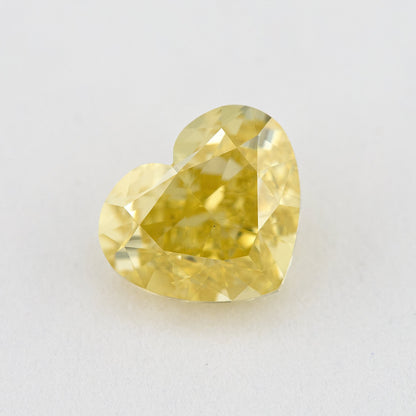 Heart-shaped yellow natural diamond face-up on a pale surface, with its lobes, point and broad crown facets visible.