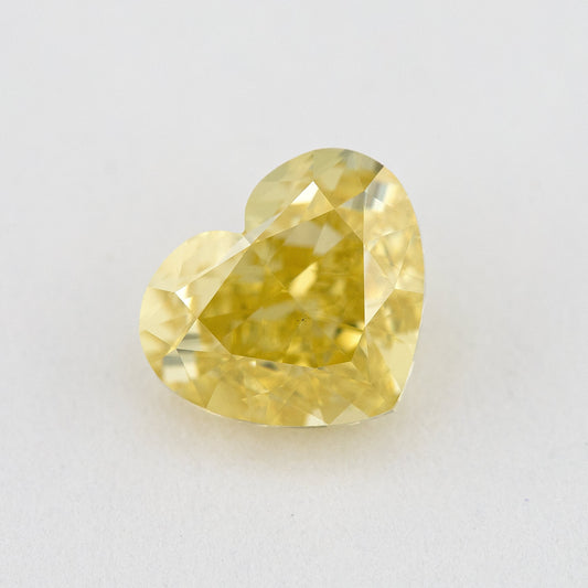 Heart-shaped yellow natural diamond face-up on a pale surface, with its lobes, point and broad crown facets visible.