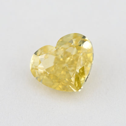 Yellow heart-shaped natural diamond tilted on a pale surface, showing the crown facets and pointed outline.