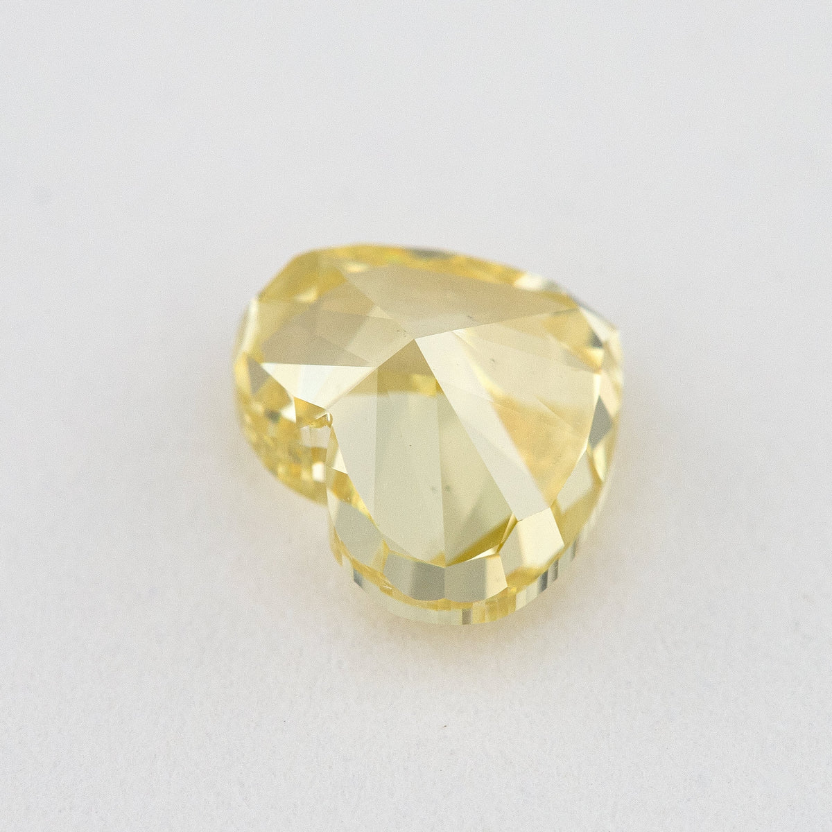 Back view of the yellow heart-shaped natural diamond on a pale surface, showing large pavilion facets.