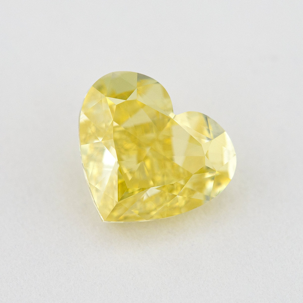 Face-up close-up of the yellow heart diamond on a pale background, showing its complete outline and crown facet reflections.