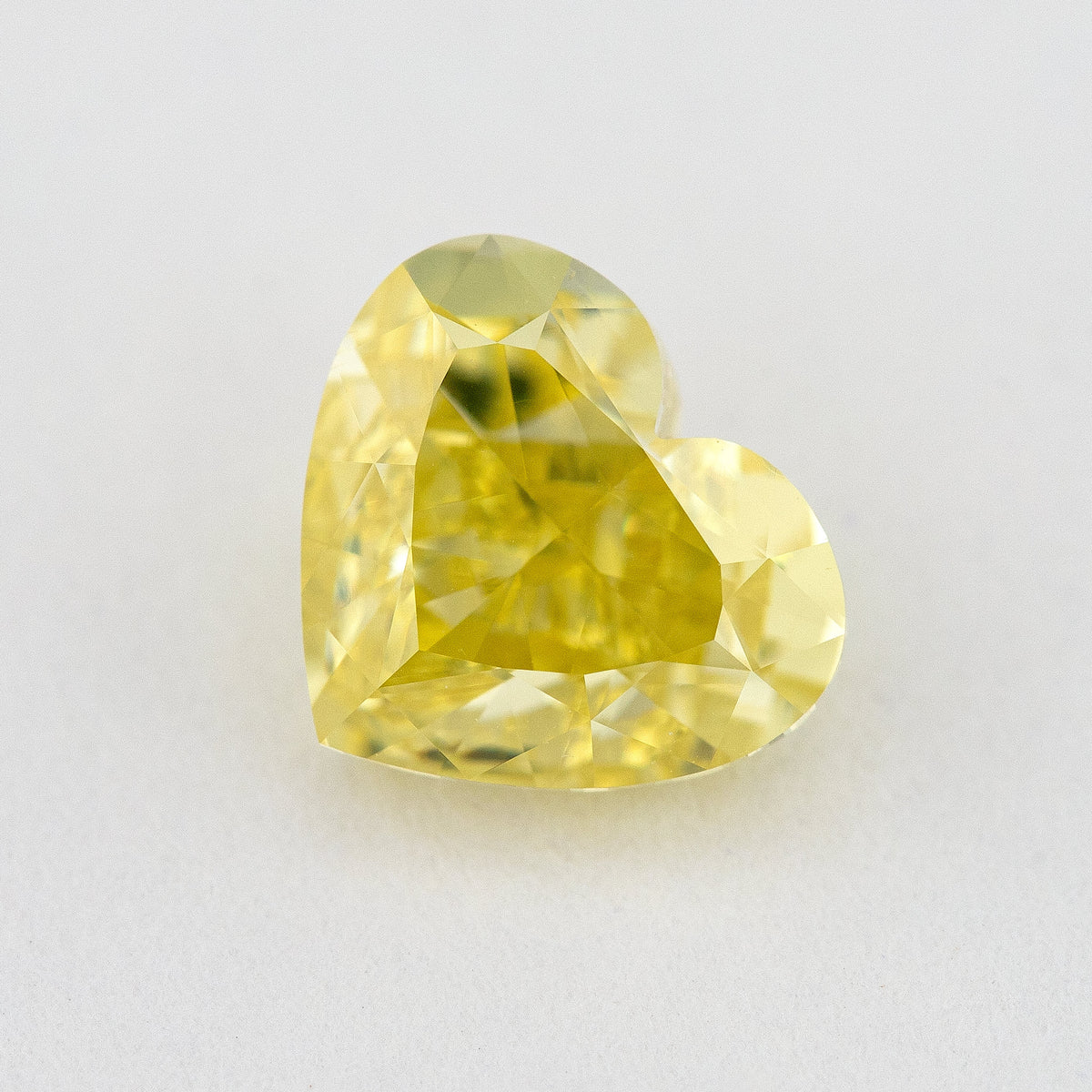Alternate angled face-up view of the yellow heart diamond on a pale background, with a different pattern of light and dark facet reflections.
