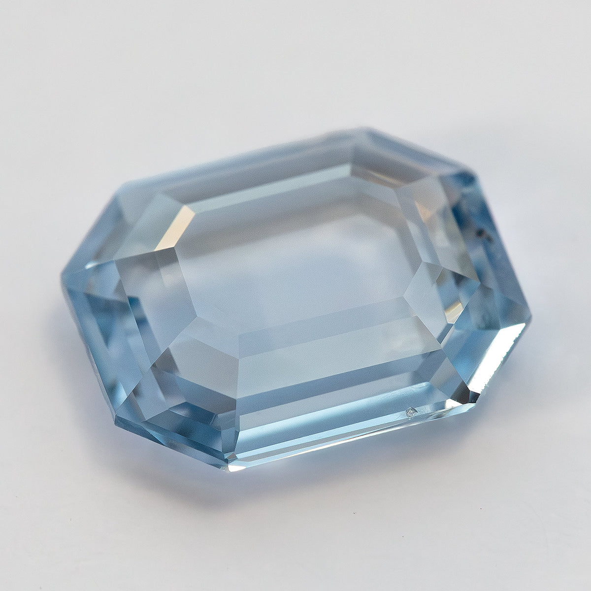 Oblique angle view of octagonal step cut light blue sapphire displaying facet reflections on white background.