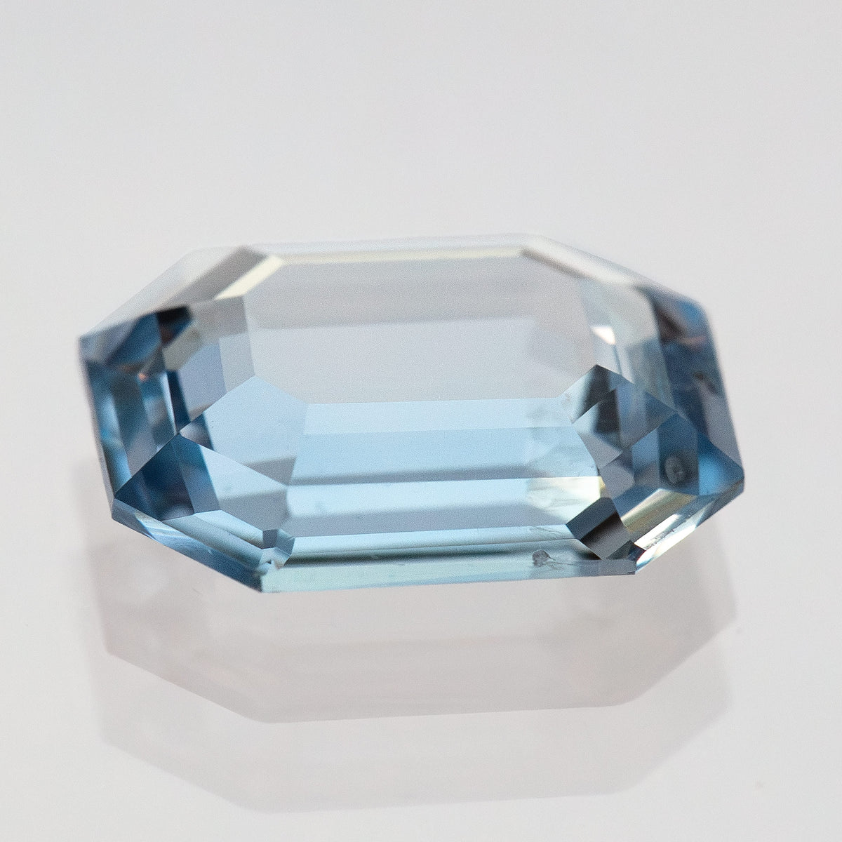 Low-angle view of transparent light blue octagonal sapphire showing facet planes and reflections.