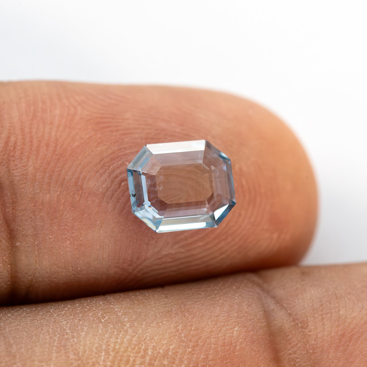 Light blue octagonal step cut sapphire resting face-up on a finger to indicate scale.