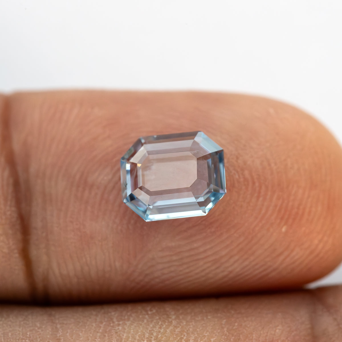 Opposite side facet pattern of light blue octagonal sapphire displayed on a finger.