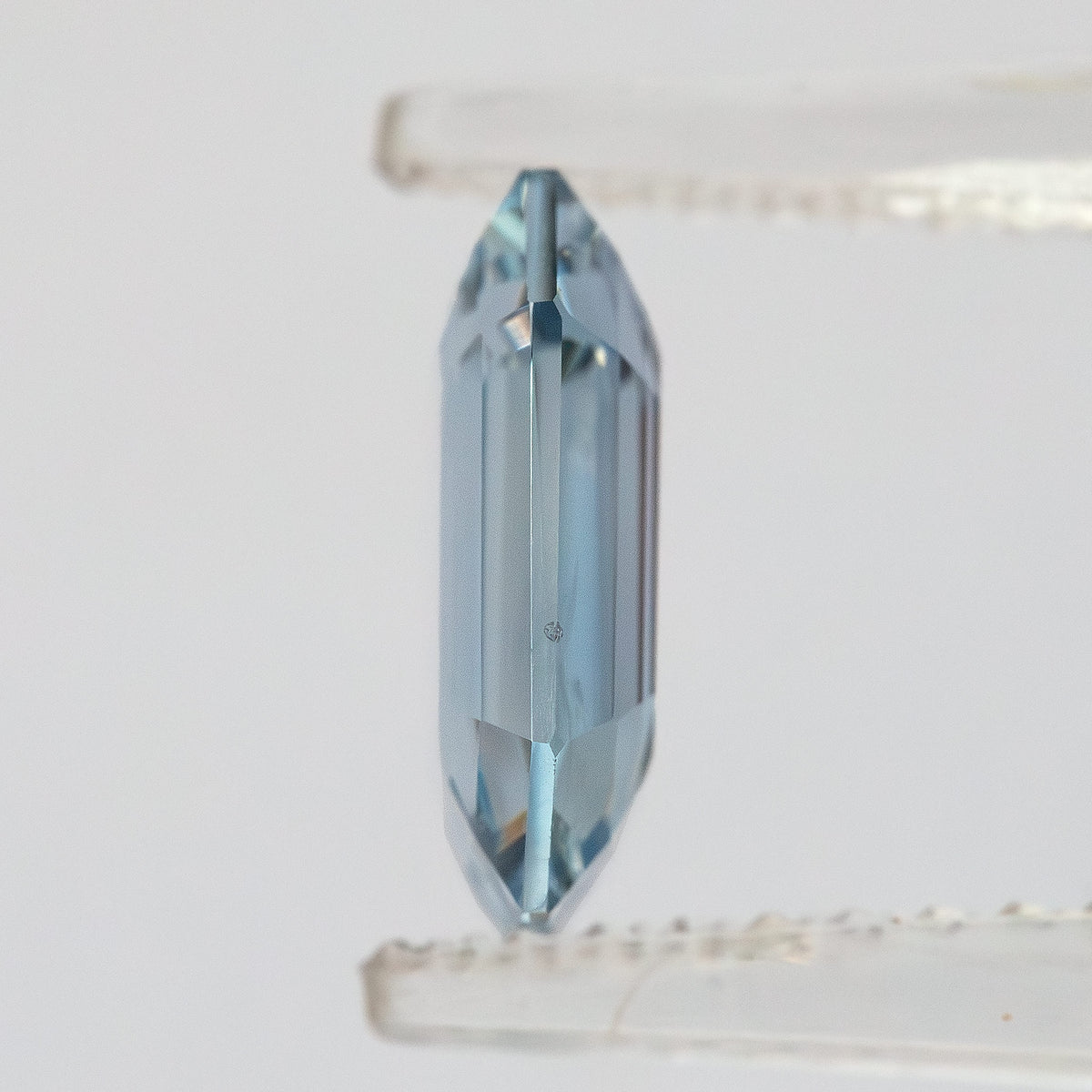 Side profile view of shallow octagonal sapphire held in tweezers revealing thin profile.