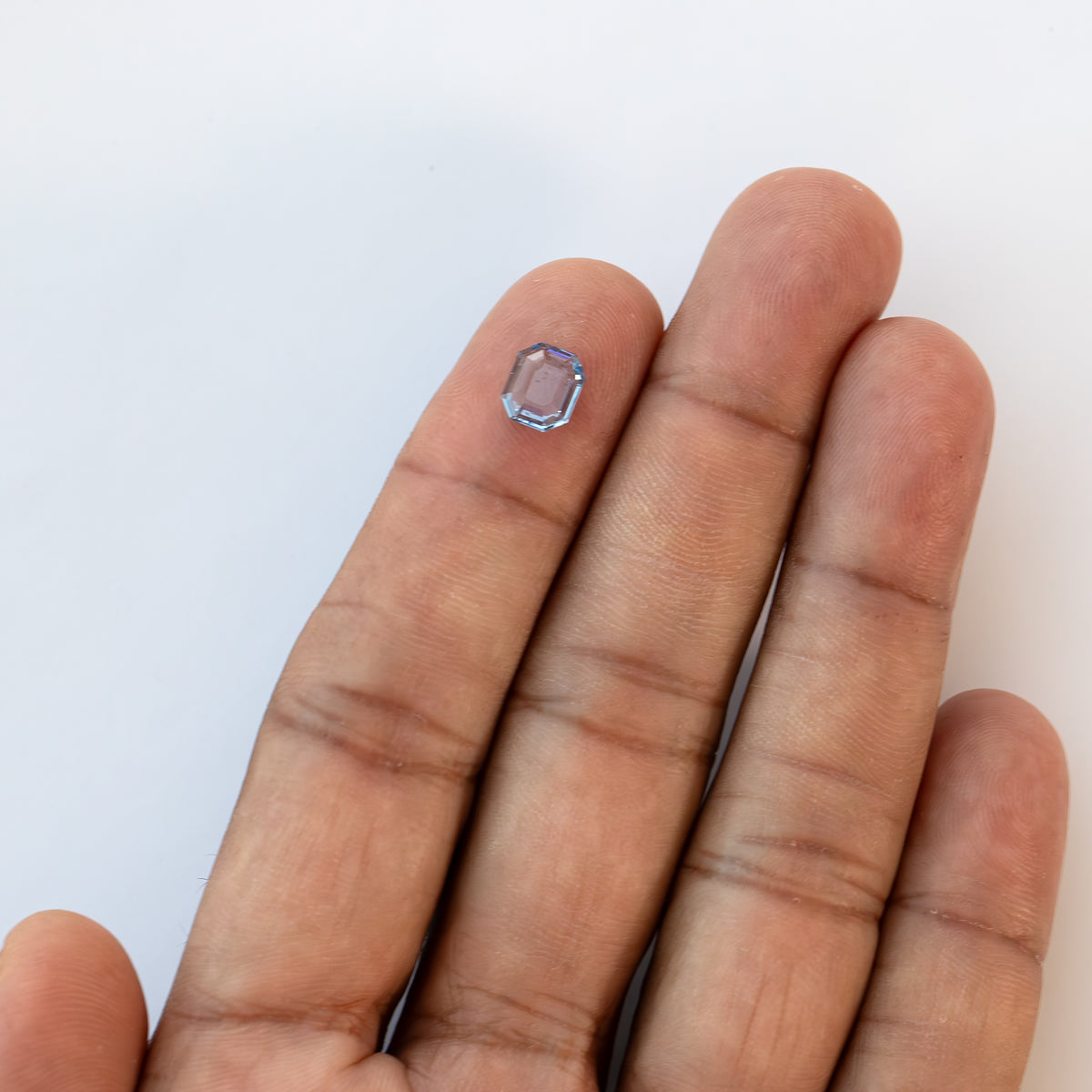 Wide view of small light blue octagonal sapphire resting on an open hand showing overall scale.