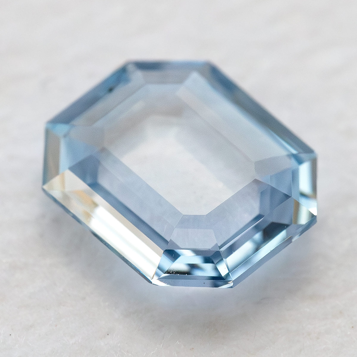 Oblique view of octagonal light blue sapphire resting on an off-white background.