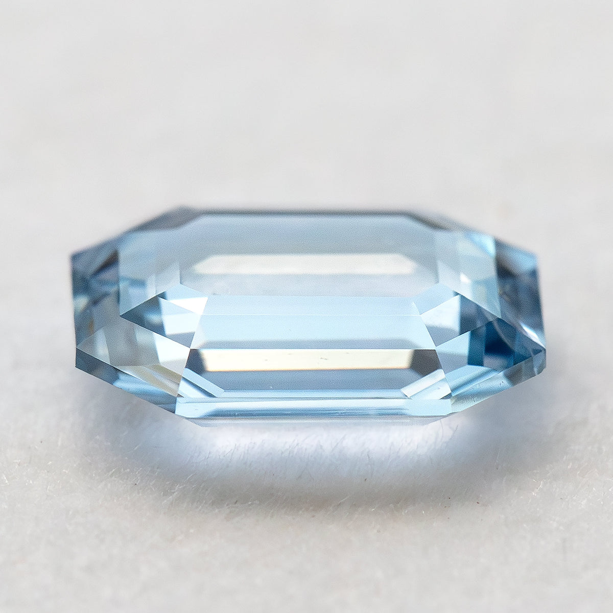 Low-angle edge view of light blue sapphire highlighting shallow proportions and side facets.