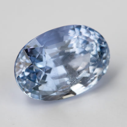 Angled face-up view of the light blue sapphire on a pale background, showing a different pattern of bright and softer reflections.