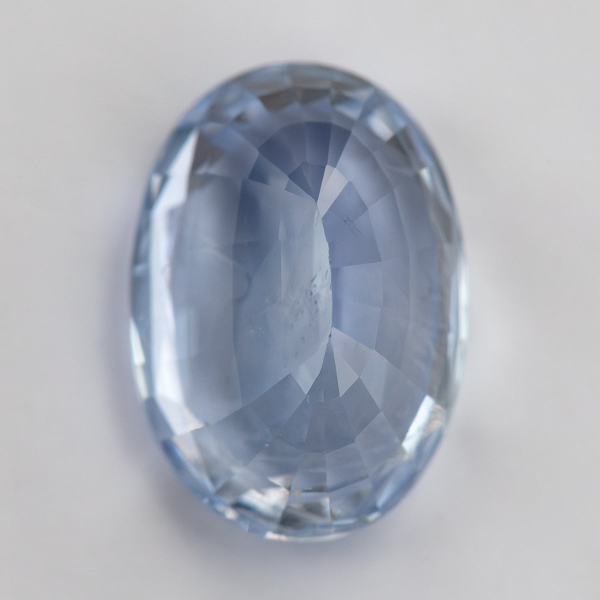 Rotated face-up view of the oval sapphire on a pale surface, showing its elongated proportions and softer reflections.