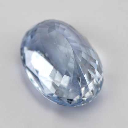 Tilted view of the light blue oval sapphire, showing crown facets, body color and depth from an oblique angle.