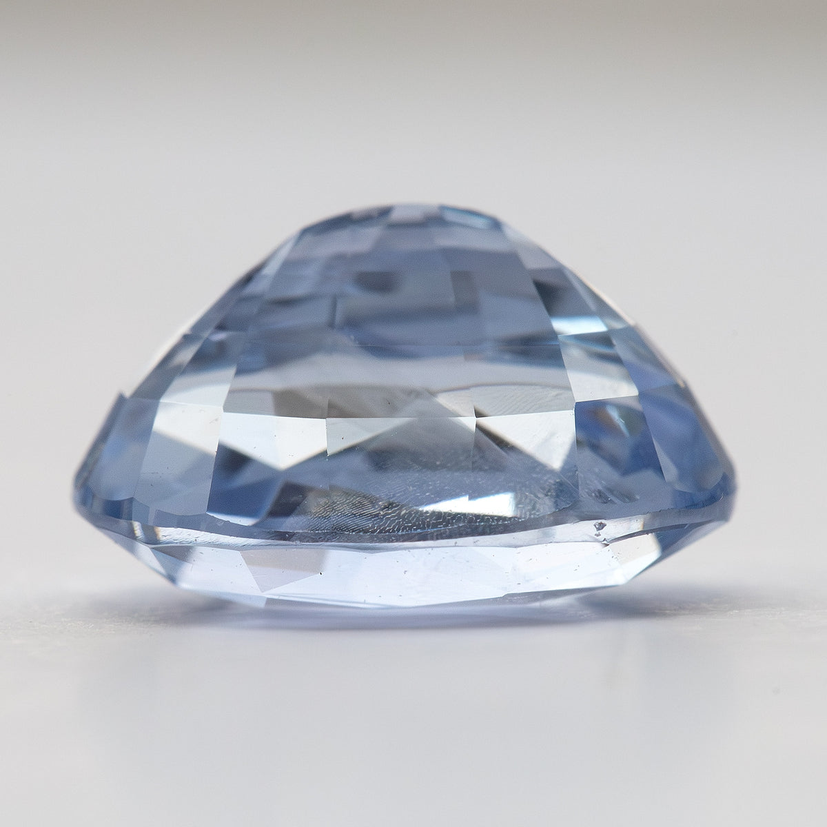 Side profile of the loose oval sapphire, showing the crown, girdle and pavilion depth against a pale background.
