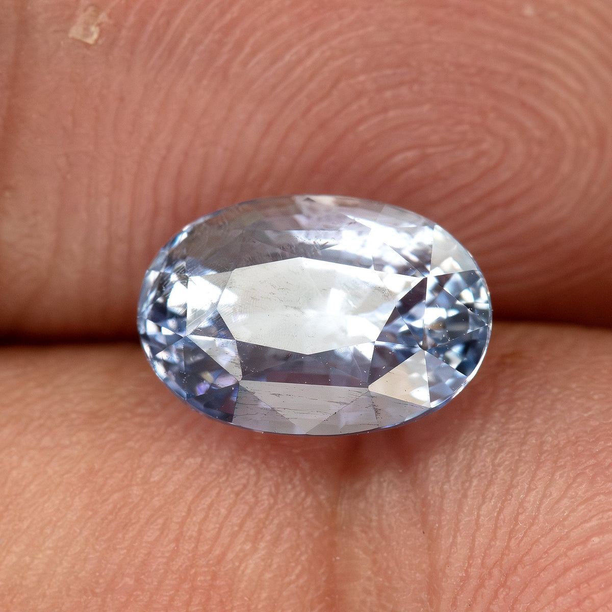 Pavilion-facing sapphire resting on a fingertip, showing the back facet arrangement and pale blue transparency.