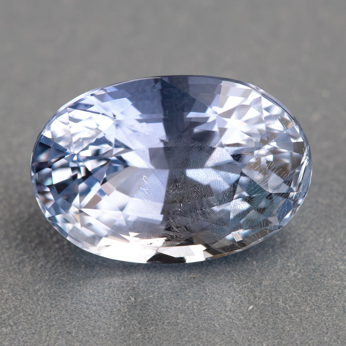 Face-up oval sapphire on a gray background, showing the pale blue body color and reflective facet pattern.