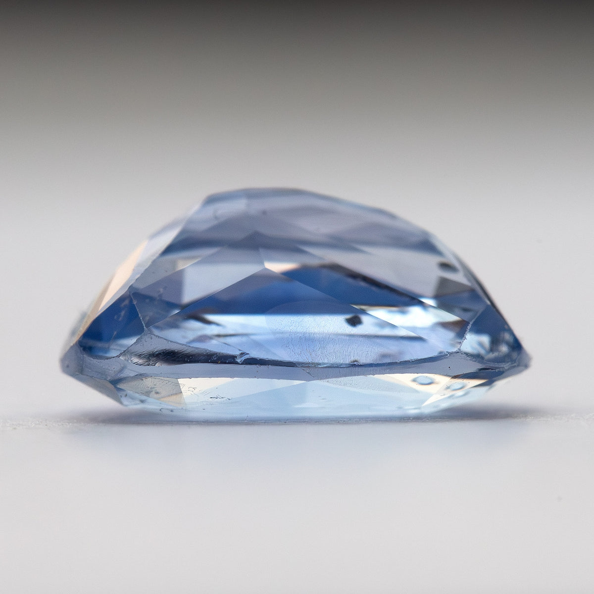 Perfil lateral del zafiro de cojín azul claro sobre blanco, mostrando la profundidad de la corona y del pabellón con una inclusión visible cerca del filetín.