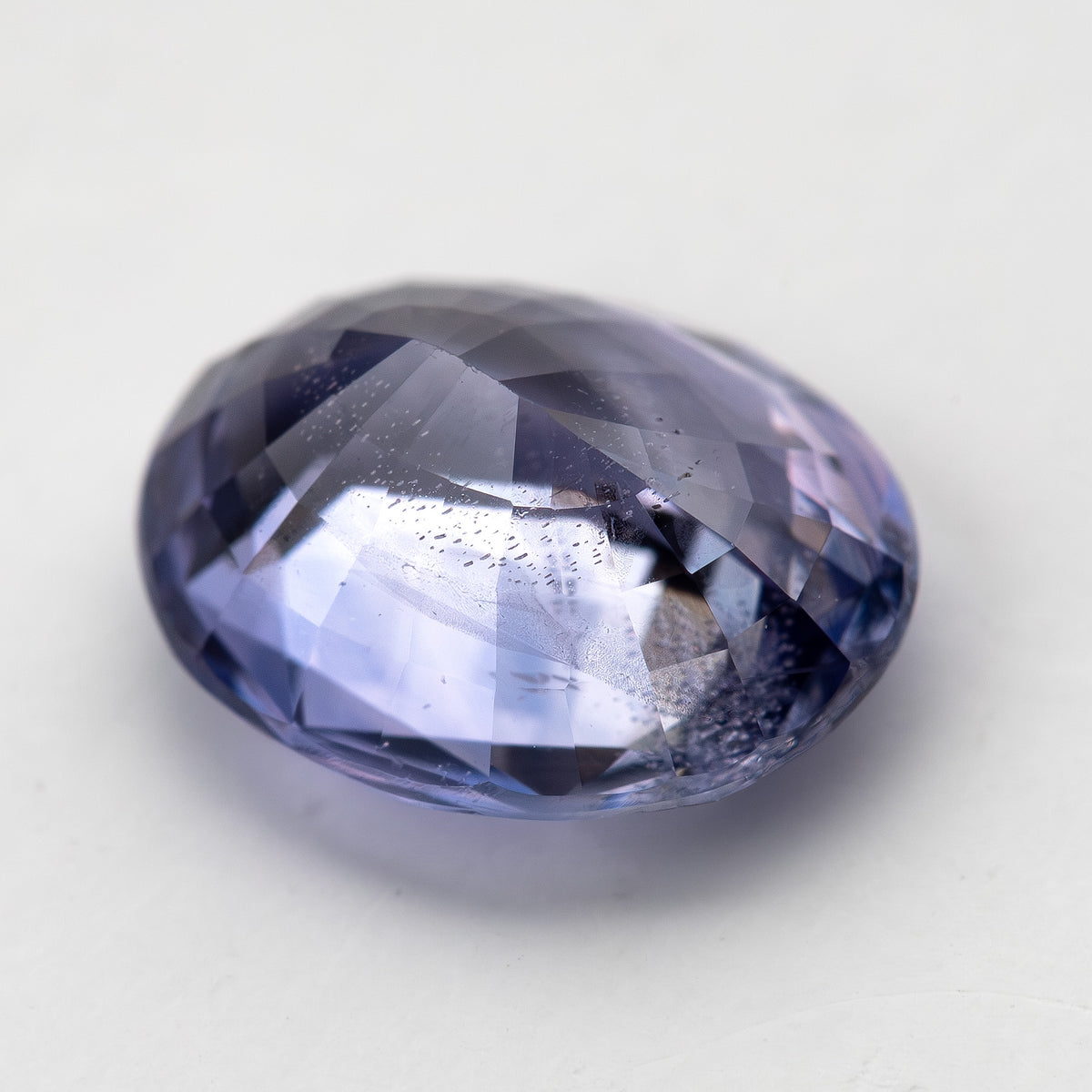 Lavender-blue oval sapphire with visible inclusions tilted face-up, showing changing light reflections. View 12.