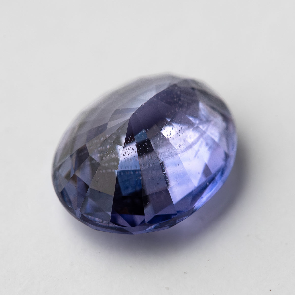 Lavender-blue oval sapphire with visible inclusions shown at an angle from the pavilion side. View 15.