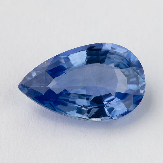 Face-up macro of a medium-light violetish blue pear mixed-cut sapphire, showing its pointed outline, pale blue table and deeper blue facet reflections.
