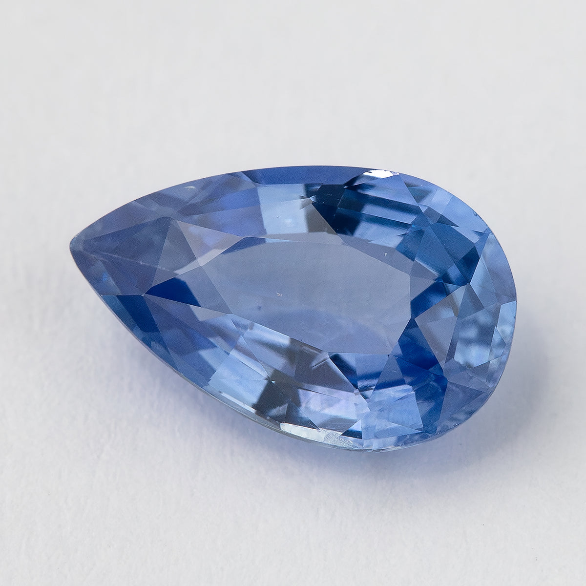 Rotated face-up view of the pear mixed-cut sapphire, with a light violet-blue center, darker blue edge facets and a few tiny visible pinpoints.