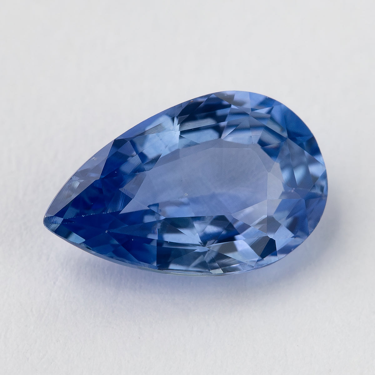 Angled face-up view of the violetish blue pear sapphire, showing deep blue flashes near the pointed end and a broad lighter blue table reflection.
