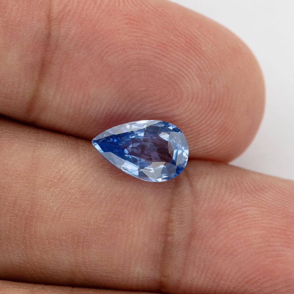Alternate hand-scale angle of the pear mixed-cut sapphire, with bright icy-blue facets, deeper blue flashes and a purplish central reflection.