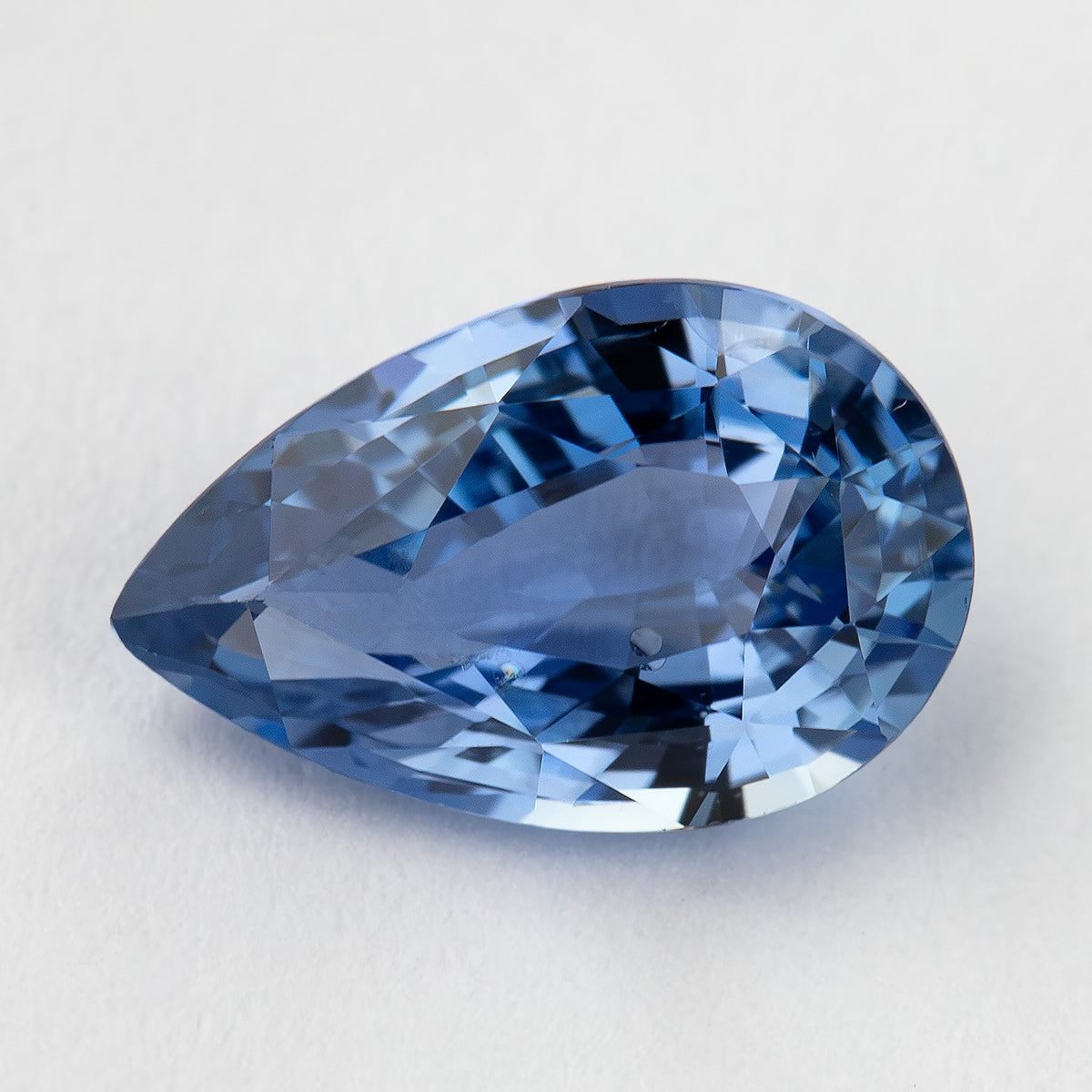 Angled macro of the light blue pear sapphire, with medium-blue flashes and small visible marks.