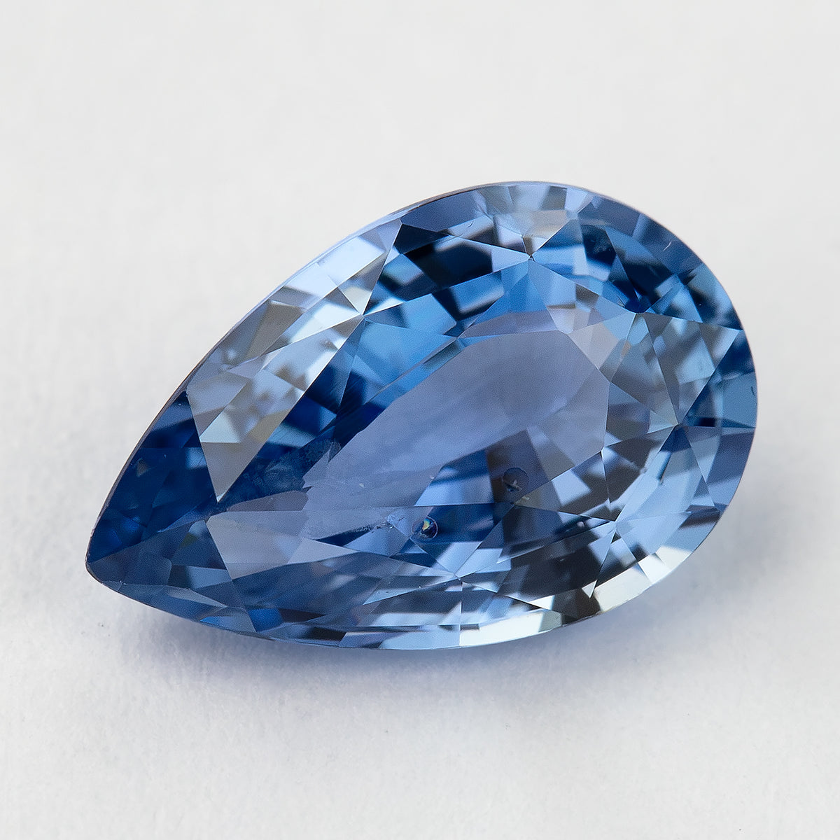 Oblique close-up of the pear sapphire, showing medium-blue flashes, mixed facets and small visible marks.