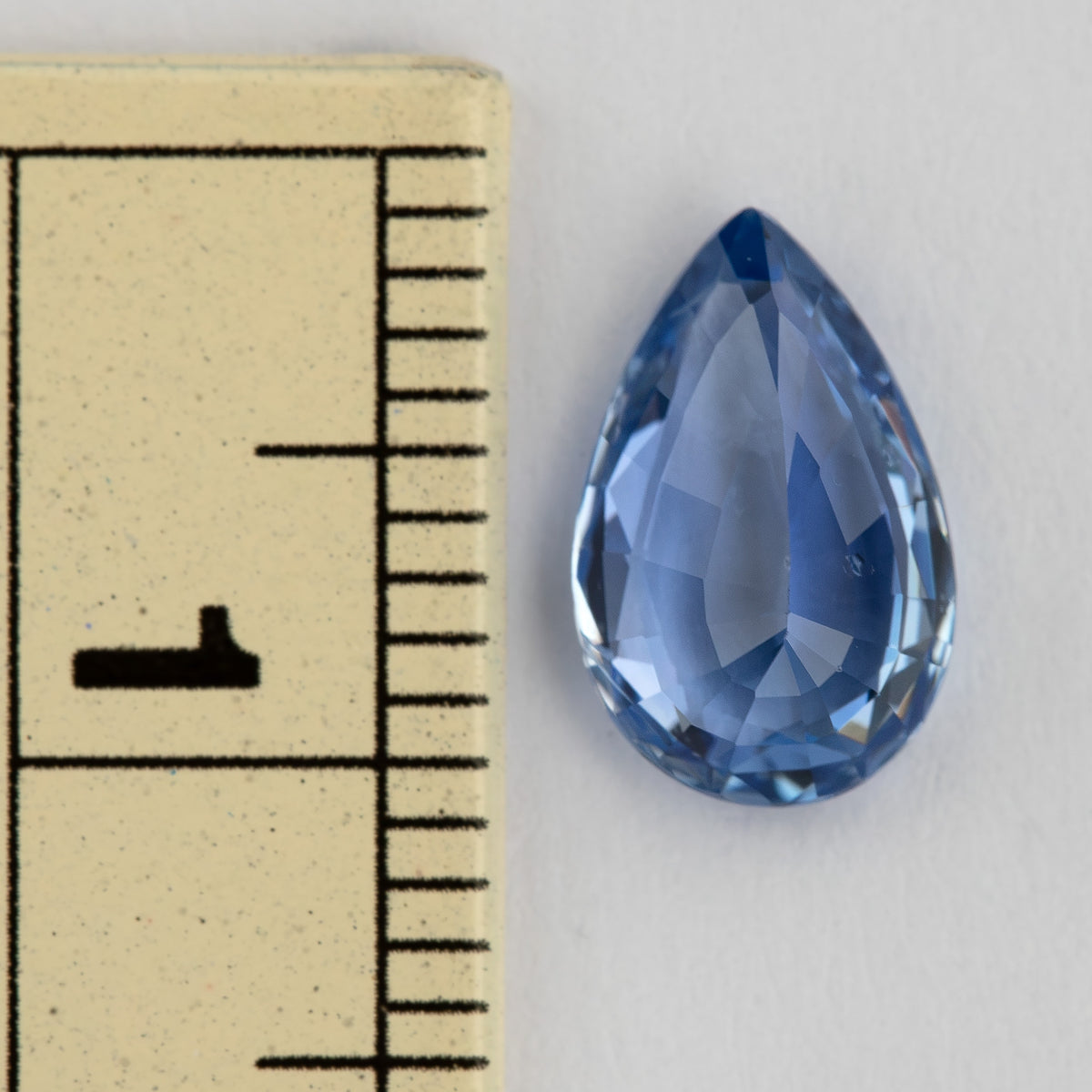 Pear-shaped light blue sapphire beside a millimeter ruler for scale, showing its 9.78 mm length and elongated outline.