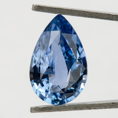 Pear-shaped light blue sapphire held vertically in metal tweezers, showing its face-up outline and mixed-cut facet pattern.