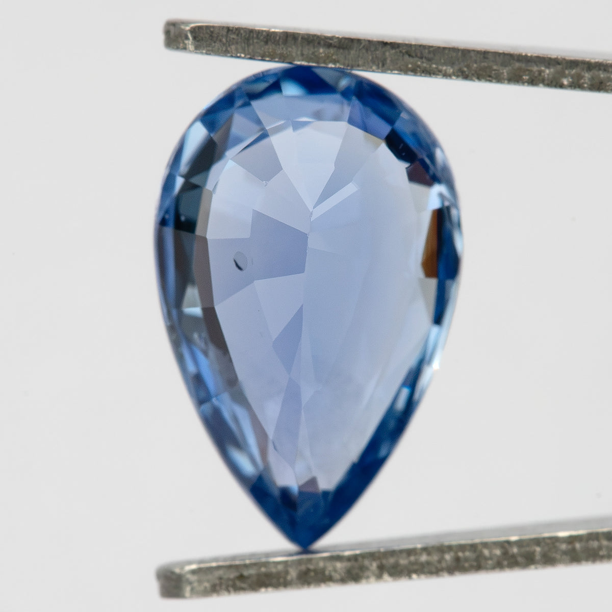 Pavilion view of the light blue pear sapphire in tweezers, showing back facets and the pointed tip.