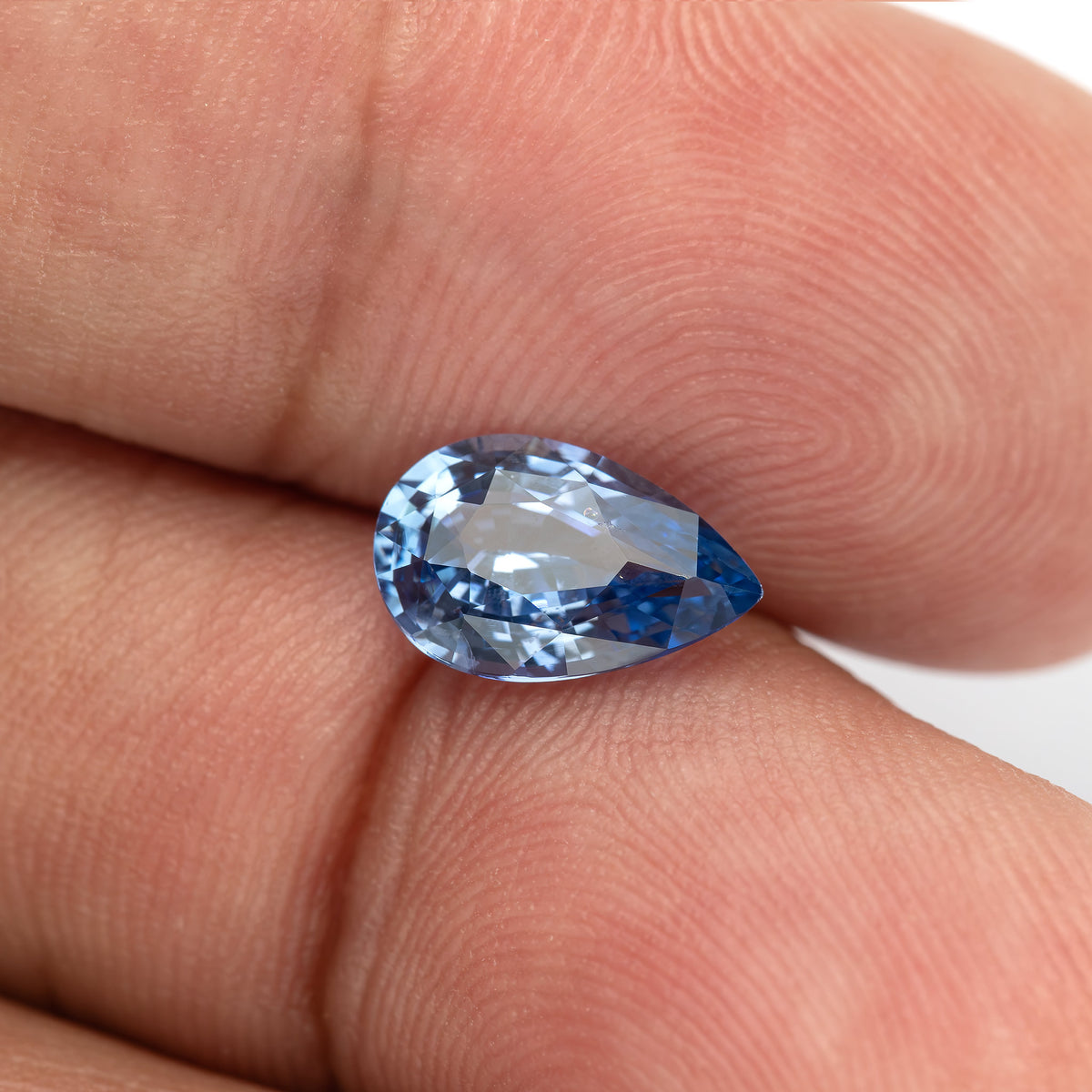 Light blue pear sapphire between fingertips for scale, showing broad face-up facets.