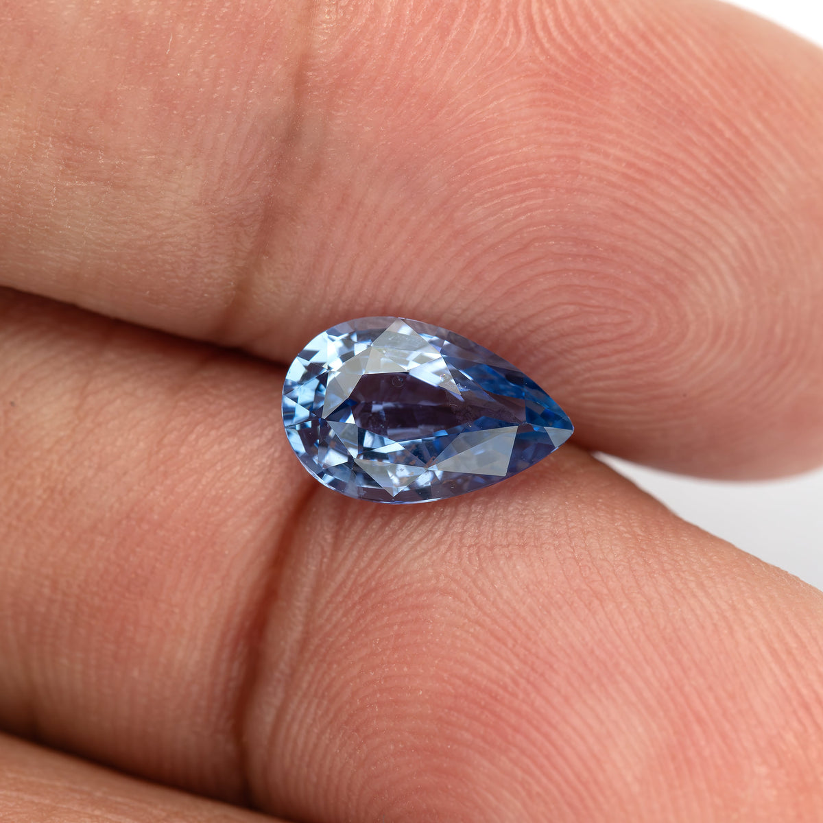 Pear sapphire between fingers for scale, showing its curved end, pointed tip and changing blue reflections.