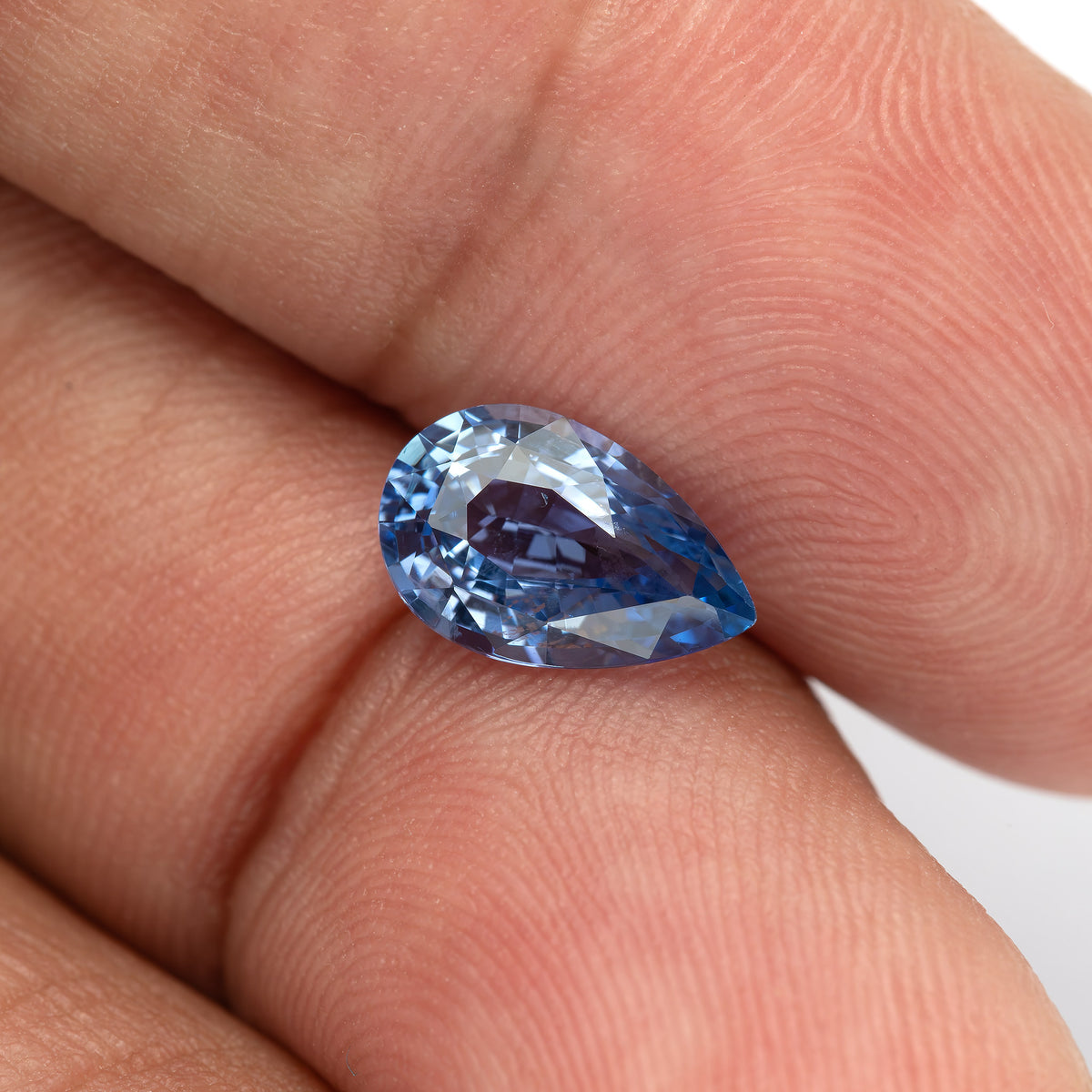 Finger-scale view of the pear sapphire, showing deeper blue reflections near its pointed end.
