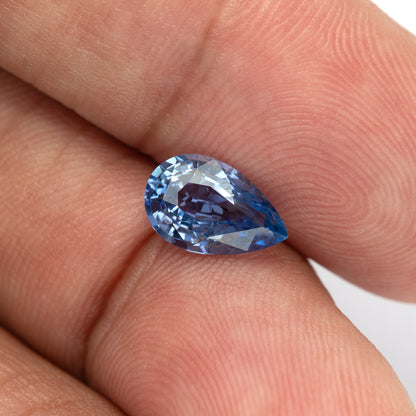 Finger-scale view of the pear sapphire, showing deeper blue reflections near its pointed end.