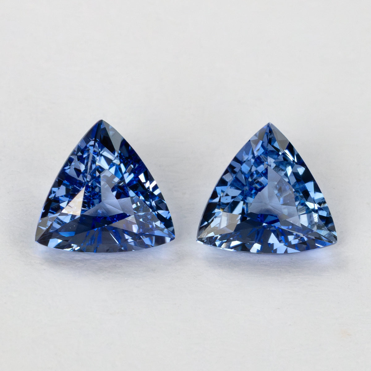 Two blue trillion-cut gemstones lying side-by-side on a white surface.