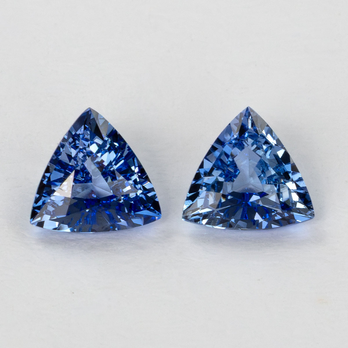 Close-up of two blue trillion-cut gemstones side-by-side on a white surface.