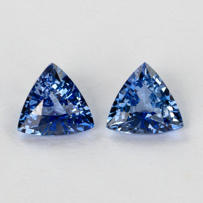 Close-up of two blue trillion-cut gemstones side-by-side on a white surface.