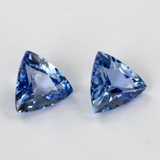 Two blue trillion-cut gemstones, one slightly angled, on a white surface.