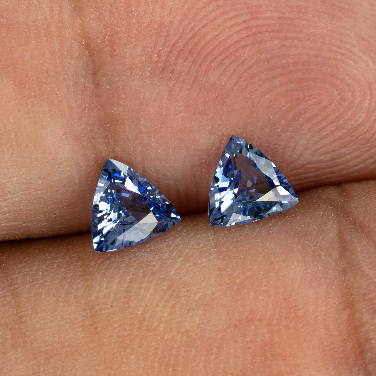 Two blue trillion-cut gemstones held between fingers, showing scale.