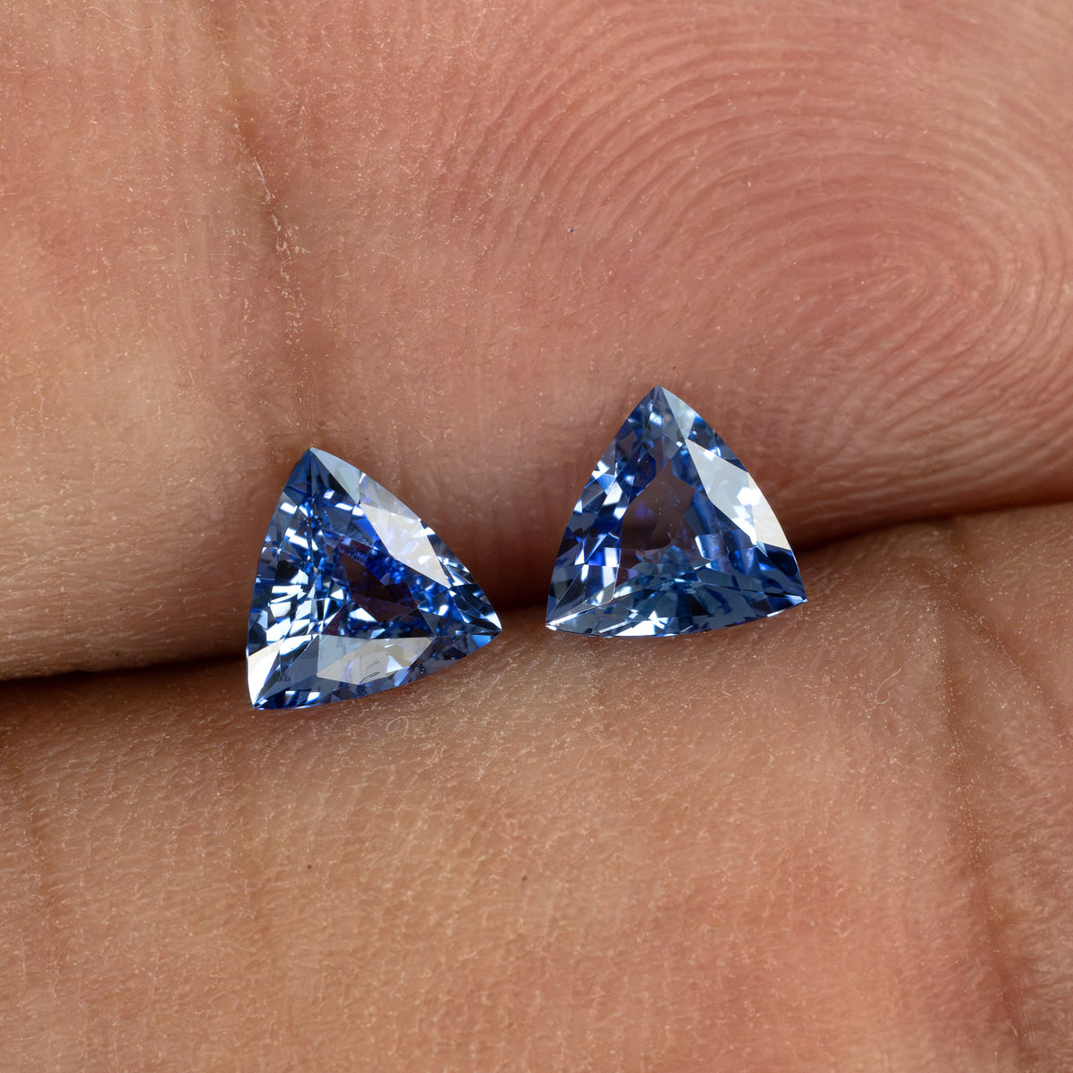 Two blue trillion-cut gemstones held between fingers, top-down view.