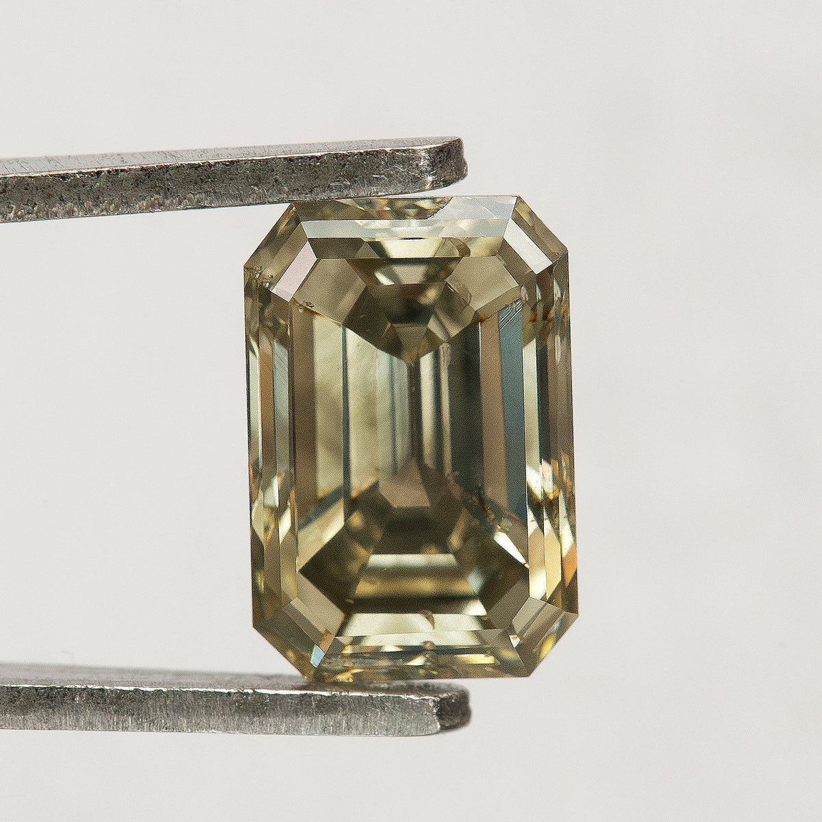 Neutral-background face-up view of the emerald-cut diamond, with bright border facets, dark central reflections and an unobstructed outline.