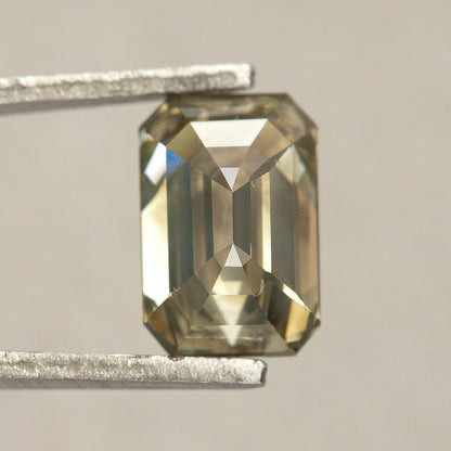 Reverse-facing emerald-cut diamond in tweezers, showing broad pavilion facets and a central lengthwise facet junction.