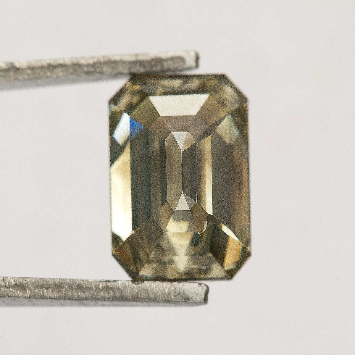 Close reverse view of the emerald-cut diamond on a pale background, showing elongated pavilion facets beneath the clipped-corner outline.
