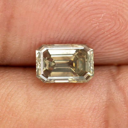 Horizontal fingertip view of the emerald-cut diamond at a changed angle, with pale step-facet reflections and darker internal areas.